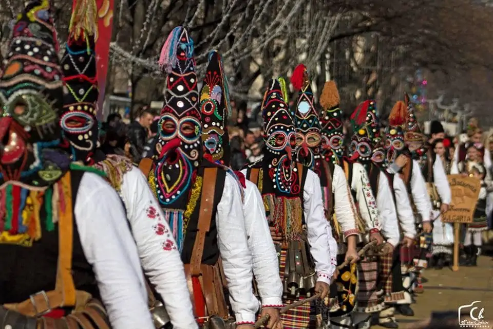 Traditional Bulgarian Kukeri procession with masked performers in elaborate costumes carrying cowbells during the Surva festival